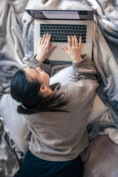 Eine Frau arbeitet im Bett an einem Laptop, Draufsicht. — Stockfoto