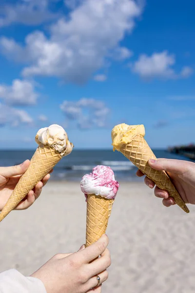 Мороженое в вафельных рожках в женских руках на фоне моря. — стоковое фото