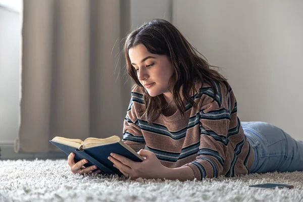 Evde yerde uzanmış kitap okuyan genç bir kadın.. — Stok fotoğraf