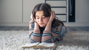 Sevimli genç bir kadın evinde yerde yatarken kitap okuyor, boşluğu kopyalıyor..