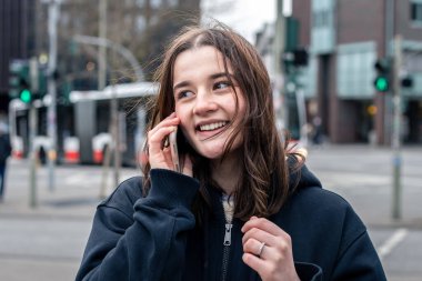 Şehirde neşeli genç bir kadın telefonda konuşuyor..