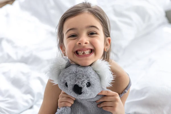 Feliz niña con juguete suave koala en la cama. — Foto de Stock