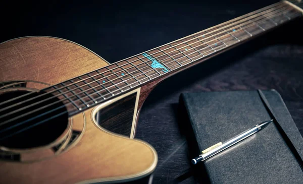 Close-up, acoustic guitar and notepad on a dark background. — Stock Fotó