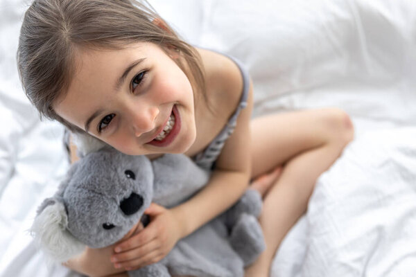 Happy little girl with soft toy koala in bed.