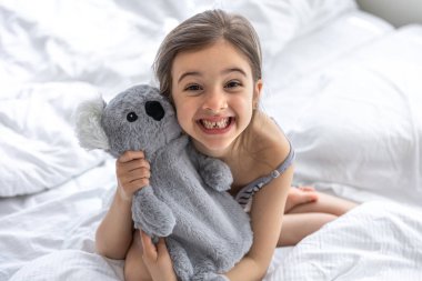 Yatakta yumuşak oyuncak koalası olan mutlu küçük kız..