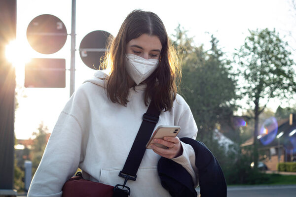 A young teenage woman is waiting for a bus at a bus stop early in the morning.