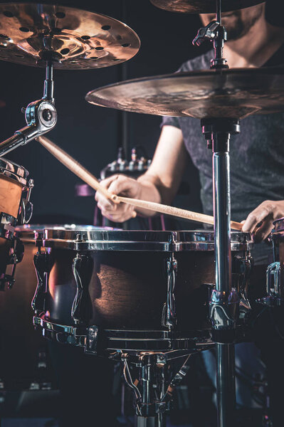 A male drummer plays the drums in a dark room.