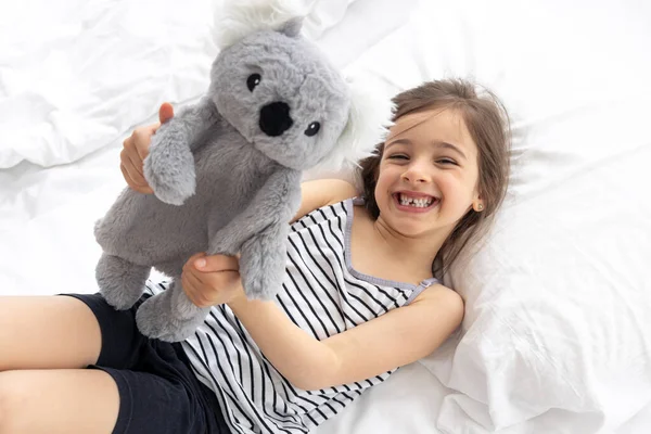 Happy little girl with soft toy koala in bed.