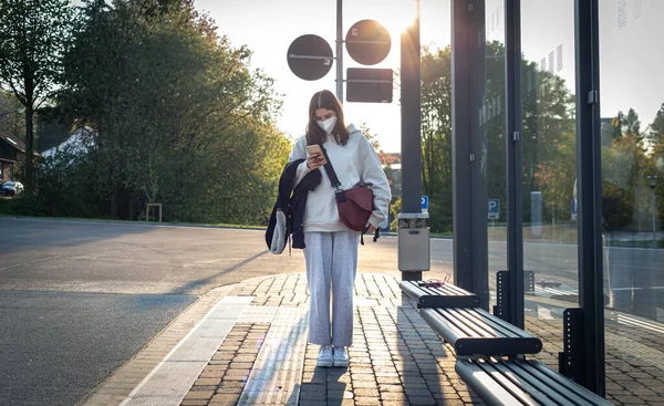 A young teenage woman is waiting for a bus at a bus stop early in the morning. — 스톡 사진