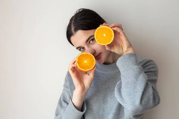 Una joven con las mitades apetitosas de una naranja sobre un fondo blanco. — Foto de Stock