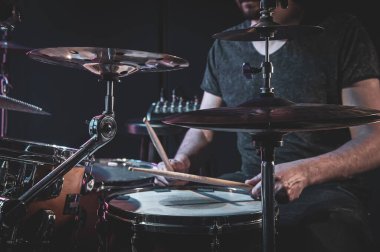 A male drummer plays the drums in a dark room.