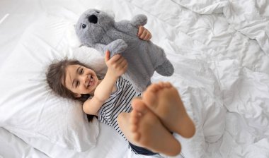 Yatakta yumuşak oyuncak koalası olan mutlu küçük kız..