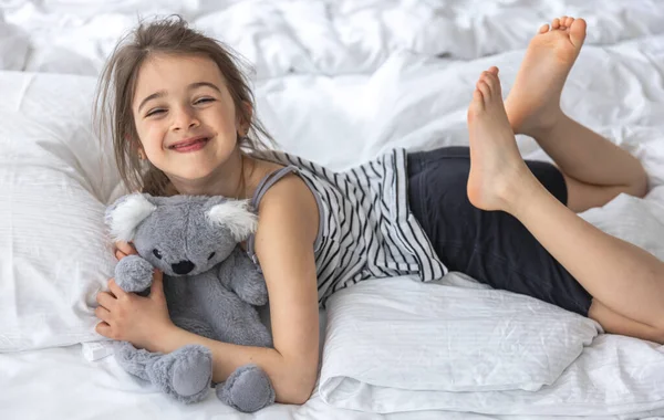 Happy little girl with soft toy koala in bed. — Stock Photo, Image