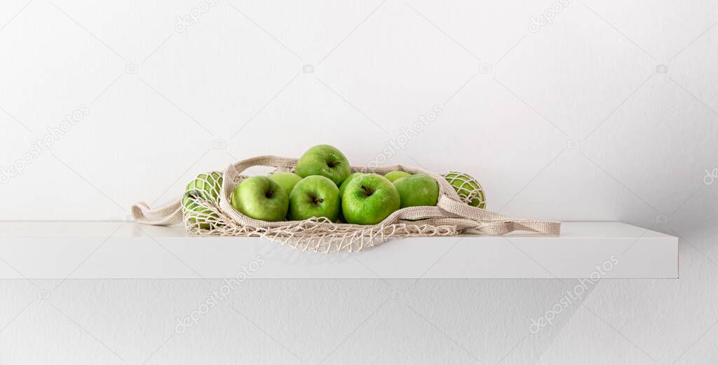 Green apples in a string bag on a white background.