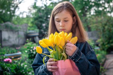 Pembe bir kesekağıdında sarı laleler olan küçük bir kız..
