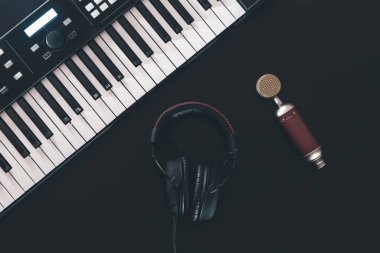 Piyano tuşları, siyah arkaplanda sentezleyici, mikrofon ve kulaklık, müzik yapma konsepti, düz konum.