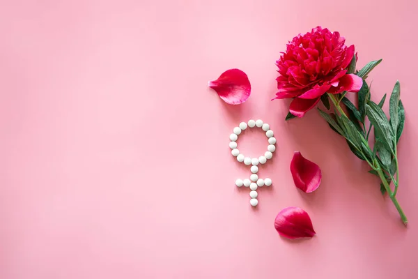 Gender Venus symbol made of pills, and peony flower on a pink background, flat lay.