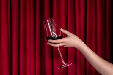 Tiyatro perdelerinin kırmızı desenli arka planında bir kadın elinde bir bardak kırmızı şarap..