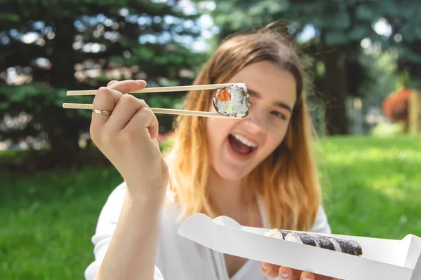 Attractive young woman eating sushi in nature, summer picnic, maki rolls.