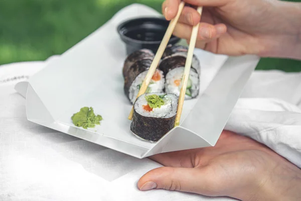 Close up, woman eating sushi in nature, summer picnic concept, maki rolls.