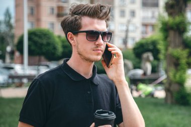 Güneş gözlüklü çekici genç adam yazın şehirde akıllı bir telefonla konuşuyor..