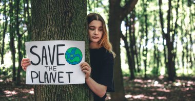 Genç bir kadın, ormandaki gezegeni, doğayı, temizliği, geri dönüşümü ve ekolojiyi kurtarma çağrısını içeren bir poster tutuyor..