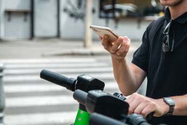 Elektrikli scooter ve cep telefonu. Şehir caddesi ve parkında kiralık bir motosikletle gezen bir adam, yaz aylarında cep telefonu kiralayarak çevre taşımacılığı yapıyor..