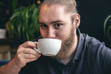 Kafede arka planda bulanık bir fincan çayla genç bir sakallı adamın portresi..