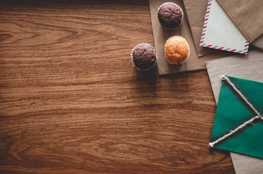 Ahşap zemin üzerinde kap kekler ve zarflarla klasik kompozisyon, düz uzanma.