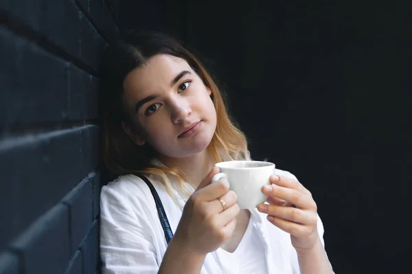 A young woman with a cup of coffee in a black cafe interior enjoys a drink, copy space.