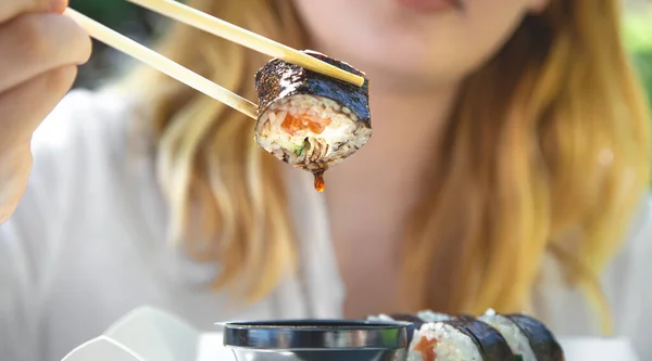 A young woman eating sushi in nature, maki roll close-up.