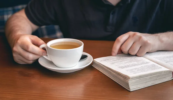 A man reads a book over a cup of tea in a cafe, close up.