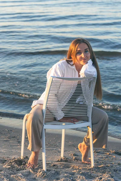 A beautiful woman is sitting on a chair near the sea, the concept of relaxation and recreation.