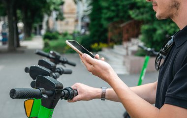 Elektrikli scooter ve cep telefonu. Şehir caddesi ve parkında kiralık bir motosikletle gezen bir adam, yaz aylarında cep telefonu kiralayarak çevre taşımacılığı yapıyor..
