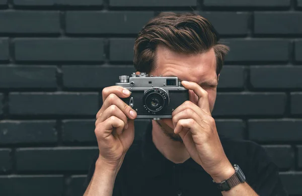 若い男が黒レンガの壁にヴィンテージフィルムカメラで写真を撮る — ストック写真