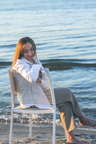 A beautiful woman is sitting on a chair near the sea, the concept of relaxation and recreation.