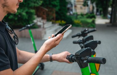 Elektrikli scooter ve cep telefonu. Şehir caddesi ve parkında kiralık bir motosikletle gezen bir adam, yaz aylarında cep telefonu kiralayarak çevre taşımacılığı yapıyor..