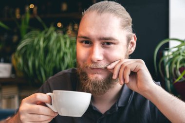 Kafede arka planda bulanık bir fincan çayla genç bir sakallı adamın portresi..