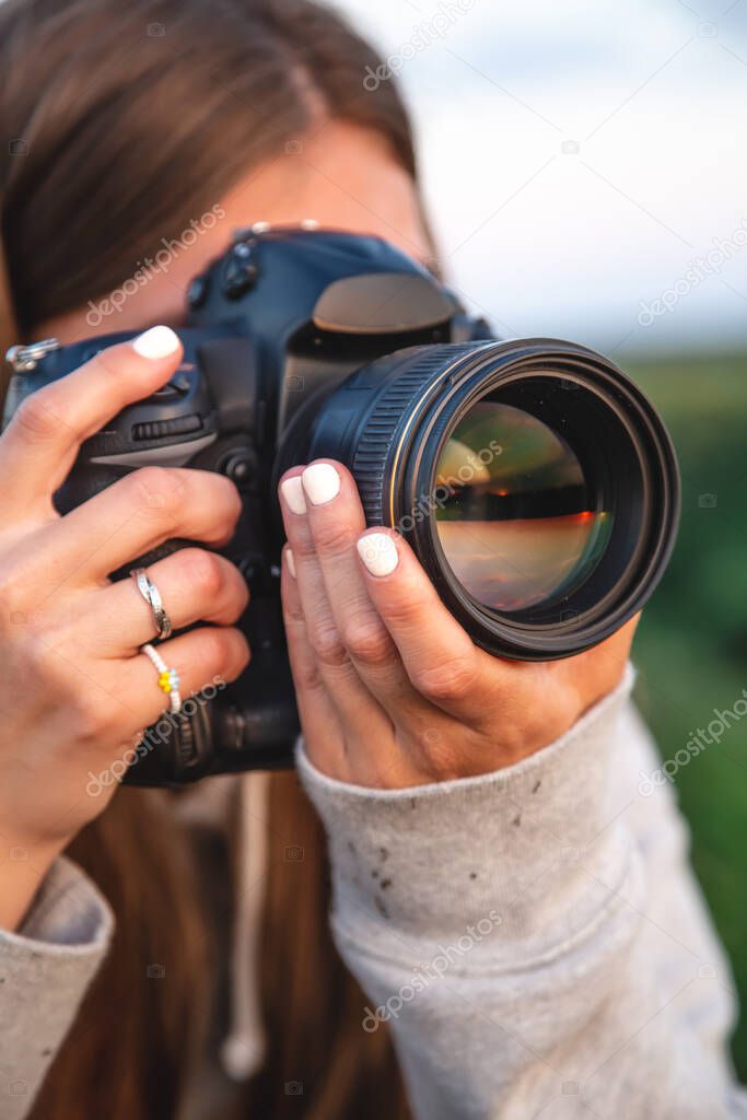 A young woman photographer with a professional camera takes a photo in nature, close-up.