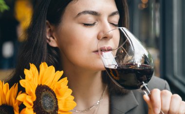 A young woman with a glass of wine and a bouquet of sunflowers in a restaurant, the concept of a date and celebration.