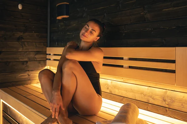 Attractive young woman is relaxing in a sauna with subdued lights.