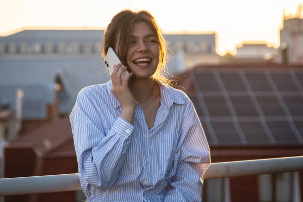 A young woman is talking on the phone on the balcony at sunset on a hot summer evening.