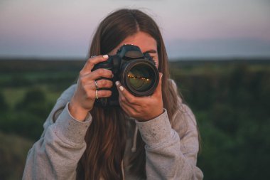 Profesyonel fotoğraf makinesi olan genç bir kadın fotoğrafçı doğada yakın plan bir fotoğraf çekiyor..