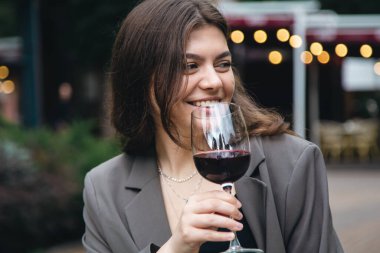 Attractive young woman with glass of red wine outside near restaurant on blurred background, party and celebration concept.