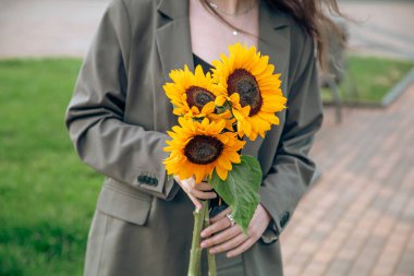 Close-up, a bouquet of sunflowers in female hands on a blurred background in the city.