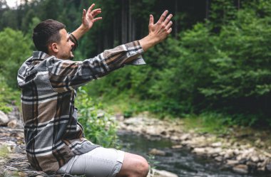 A young man in a plaid shirt in the forest by the river enjoys nature, wildlife.