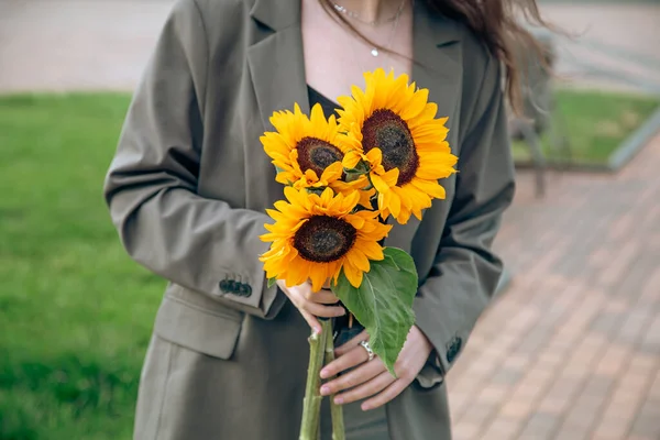 Close-up, a bouquet of sunflowers in female hands on a blurred background in the city.