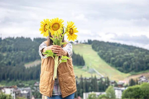 Woman with a bouquet of sunflowers in nature in the mountains, copy space.