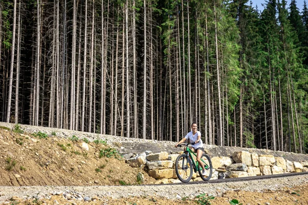 Athletic young woman rides a bike in a mountainous area in the forest, copy space.