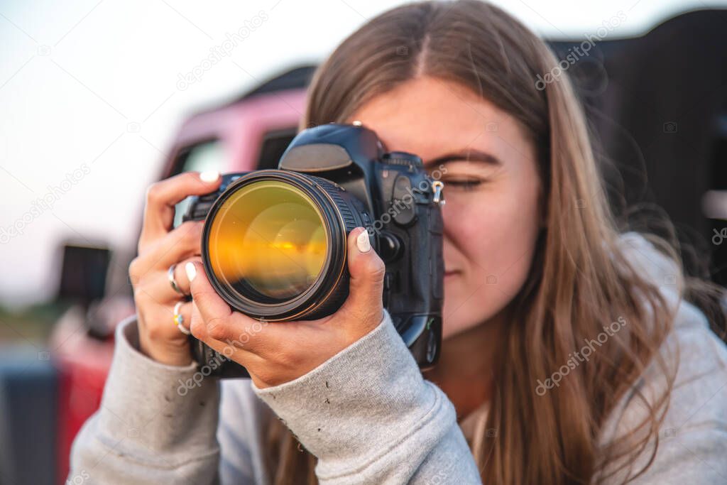 A young woman photographer with a professional camera takes a photo in nature, close-up.